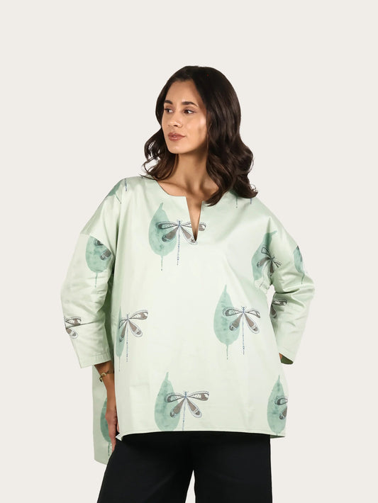 Woman wearing a light green blouse with floral patterns and black pants on a white background