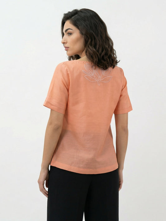 Seen Unseen warm orange cotton pleated top with floral embroidery on back and tassel ties. Short sleeves, flowing silhouette.